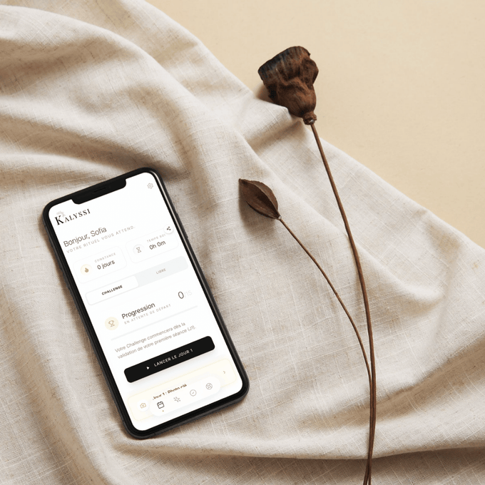 Photo d'un iPhone posé sur un drap beige avec l'application Kalyssi Compagnon beauté ouverte sur la page home.