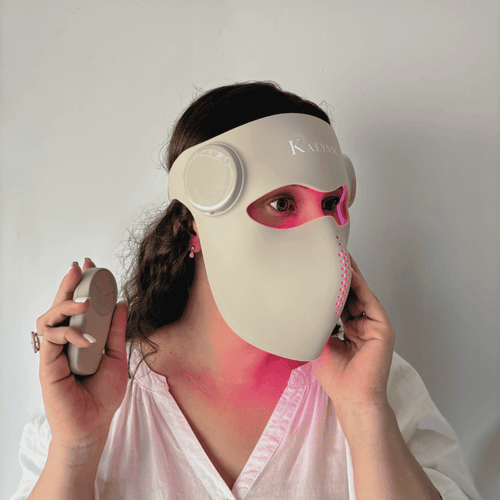 Masque LED visage Kalyssi porté par une femme, avec une lumière rose visible et une télécommande en main.